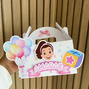 Puede incluir: Caja de regalo blanca decorada con una ni&ntilde;a de dibujos animados, globos y una caja de regalo. La caja tiene una cinta rosa y el nombre "AMARAE" en una pancarta rosa. Los globos son en tonos azules, rosas y amarillos.