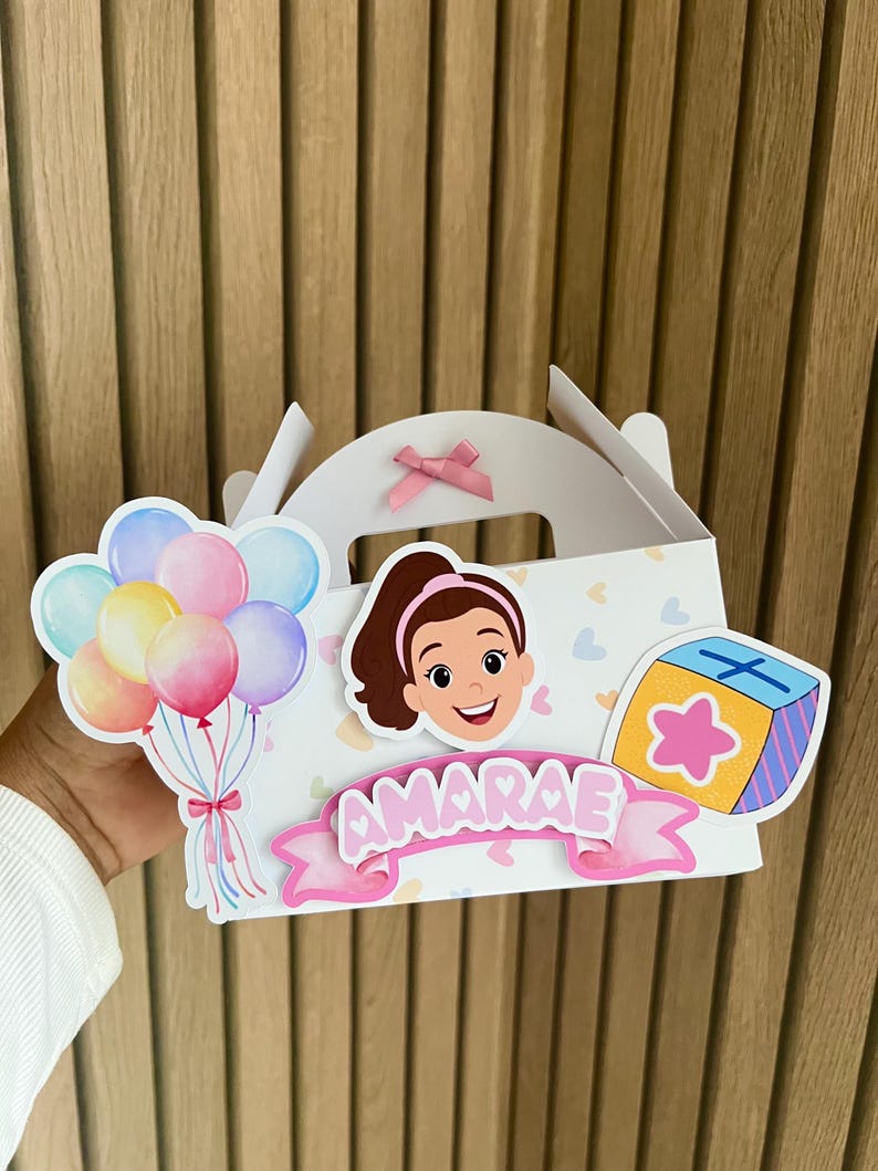 Puede incluir: Caja de regalo blanca decorada con una ni&ntilde;a de dibujos animados, globos y una caja de regalo. La caja tiene una cinta rosa y el nombre "AMARAE" en una pancarta rosa. Los globos son en tonos azules, rosas y amarillos.