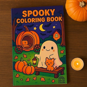 Op de afbeelding: Een "Spooky Coloring Book" met een Halloween-thema. De cover toont een spook, een kat, een pompoenwagen en pompoenen. Een brandende kaars en een pompoen zijn ook aanwezig. Het boek ligt op een houten oppervlak.