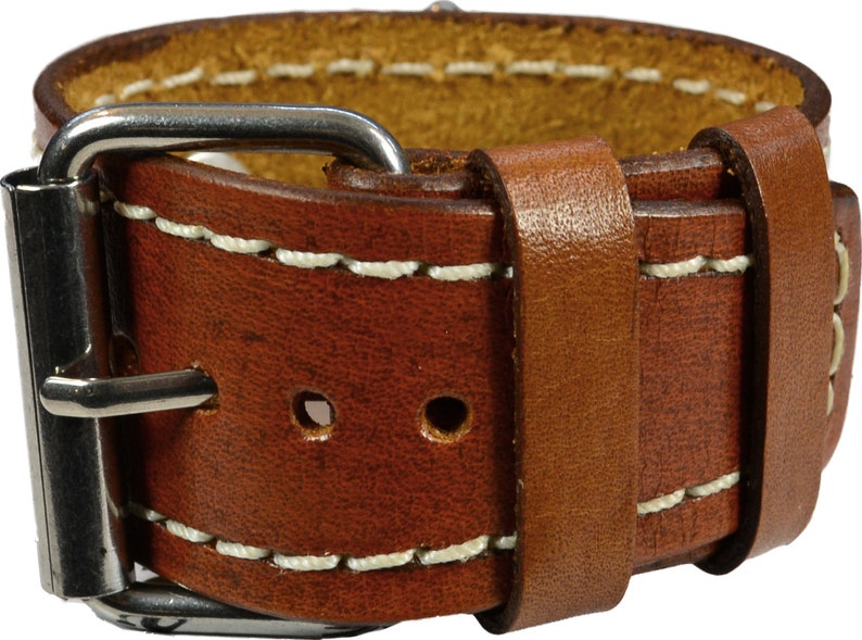 Puede incluir: Primer plano de una correa de reloj de cuero marr&oacute;n con costuras blancas y una hebilla plateada. La correa es gruesa y parece estar hecha de cuero de alta calidad. Las costuras son limpias y uniformes, y la hebilla es brillante.