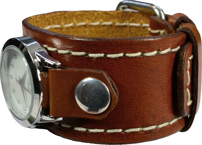Puede incluir: Un reloj de pulsera con brazalete de cuero marr&oacute;n con esfera plateada. La correa del reloj es de cuero grueso cosido con interior marr&oacute;n claro. La esfera tiene n&uacute;meros y agujas negros. La correa se asegura con una hebilla plateada y un broche plateado.