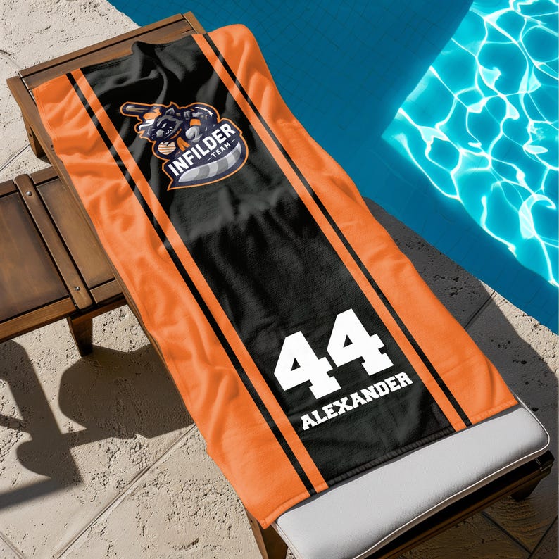 May include: An orange and black beach towel with the text "INFILDER TEAM" and the number "44" with the name "ALEXANDER". The towel is folded over a wooden lounge chair next to a pool.