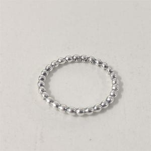 May include: A silver ring with a beaded design. The ring is made of small, round beads that are closely spaced together, creating a textured surface. The ring is on a white background. The ring has the text "925 ALE 54" engraved on it.