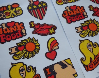 May include: Sheets of vintage stickers with retro designs. The stickers feature phrases like "I love junk food!" and "I love blonde!" in orange, red, and yellow. Other designs include hearts, lips, and a sun.