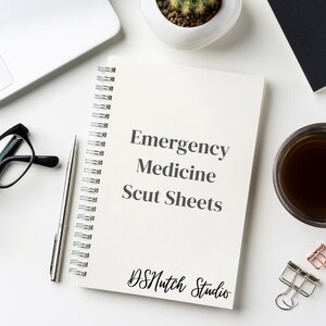 Pode incluir: Um caderno branco com espiral com o texto "Emergency Medicine Scut Sheets" e "DSMutch Studio". Uma caneta prateada, óculos com armação preta e uma xícara de café estão sobre uma superfície branca.
