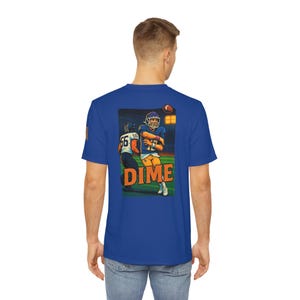 May include: Royal blue t-shirt featuring a graphic of a football player throwing a pass, with the word "DIME" in orange. The illustration shows two players in action on a green field under stadium lights.