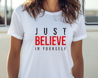 May include: A white t-shirt featuring the motivational phrase "JUST BELIEVE IN YOURSELF". The word "BELIEVE" is in red, contrasting with the black text of the other words. The shirt has short sleeves.