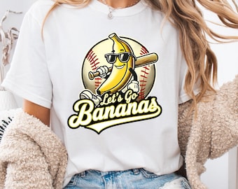 May include: White t-shirt featuring a cartoon banana wearing sunglasses and holding a baseball bat, set against a baseball. The text "Let's Go Bananas" is below the graphic. The shirt is a casual style.
