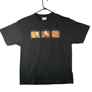 Puede incluir: Camiseta negra con tres imágenes enmarcadas: Walt Disney, Mickey Mouse y el logotipo del Milenio. Los textos "The Man", "The Mouse" y "The Millennium" están encima de cada imagen. Debajo de las imágenes está el texto "Walt Disney World".