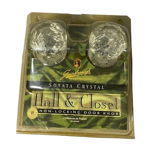 Puede incluir: Dos pomos de puerta Gainsborough Sonata de cristal transparente en un paquete de plástico. El paquete dice "Hall & Closet Non-Locking Door Knob". Los pomos tienen un diseño facetado. El paquete tiene un diseño verde y dorado.