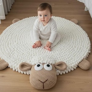 May include: A white, round, sheep-shaped rug with a crocheted head, ears, and legs. A baby in a white onesie sits on the rug. The rug is on a light brown wooden floor.