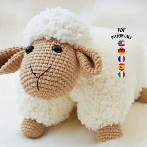 May include: A crocheted sheep toy with a fluffy white body, a tan head, ears, and legs, and black button eyes. The sheep has a smiling face. The image includes the text "PDF PATTERN ONLY" with flags.