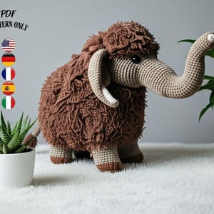 Puede incluir: Un juguete de mamut lanudo tejido a ganchillo en tonos marrones y beige, con orejas grandes y una larga trompa. El texto "PDF PATTERN ONLY" está en la parte superior. El mamut está sobre una superficie blanca, con plantas en macetas a ambos lados.