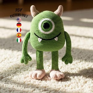 Può includere: Un mostro verde all'uncinetto con un occhio grande, piccole corna e una bocca sorridente. Il mostro ha braccia, gambe e piedi rosa. Il testo "PDF PATTERN ONLY" si trova nell'angolo in alto a sinistra.