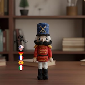 Può includere: Una bambola schiaccianoci all'uncinetto fatta a mano. La bambola ha un cappello blu con una croce dorata, una giacca rossa e stivali neri. Il testo "PDF PATTERN ONLY" è visibile. Lo sfondo include una libreria e libri.
