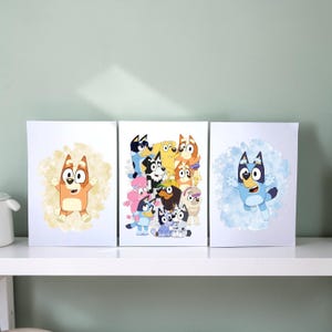 Puede incluir: Tres láminas de arte rectangulares con personajes de perros de dibujos animados. La lámina de la izquierda muestra un perro naranja sobre un fondo de acuarela amarillo. La central muestra un grupo de perros coloridos. La de la derecha muestra un perro azul sobre un fondo de acuarela azul.