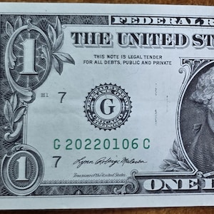 May include: A United States one-dollar bill. The bill features a portrait of George Washington in the center, with the text "ONE DOLLAR" at the bottom. The bill is green and black with the text "THE UNITED STATES OF AMERICA" at the top.
