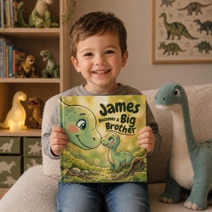 May include: A smiling child holds a book titled "James becomes a Big Brother." The book cover shows a green dinosaur illustration. A plush dinosaur toy is next to the child. The background includes a bookshelf with dinosaur figurines.