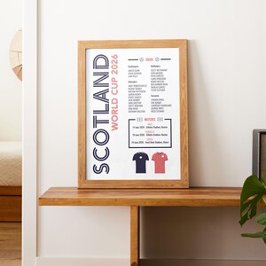 Puede incluir: Una l&aacute;mina enmarcada titulada Scotland World Cup 2026 que muestra una lista de jugadores, fechas y lugares de los partidos. El dise&ntilde;o incluye un esquema de color azul oscuro y rojo con ilustraciones de dos camisetas de f&uacute;tbol en la parte inferior.