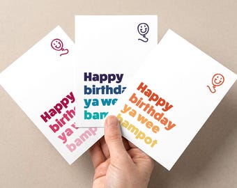 Puede incluir: Tres tarjetas de cumpleaños blancas con texto colorido e ilustraciones de globos. Las tarjetas dicen "Happy birthday ya wee bampot" en tonos rosa, azul y naranja. Cada tarjeta tiene una ilustración de globo de diferente color.