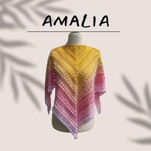 Könnte beinhalten: Ein handgefertigter Schal in einem Farbverlauf von Gelb, Rosa und Lavendel. Der Schal ist mit einem detaillierten Stichmuster gehäkelt und wird auf einer Schaufensterpuppe präsentiert. Das Wort "AMALIA" steht in schwarzen Buchstaben über dem Schal.