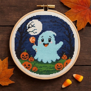 Puede incluir: Un bastidor de bordado de punto de cruz con un fantasma azul claro sosteniendo una piruleta, rodeado de calabazas naranjas y una luna llena contra un cielo nocturno azul oscuro. Perfecto para la decoración de Halloween.