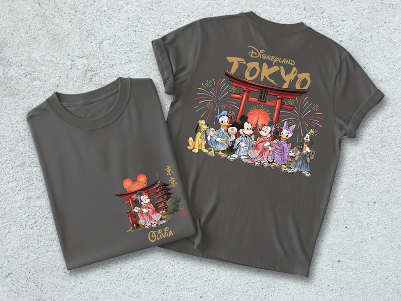 May include: Two gray t-shirts with Japanese-themed Disney designs. One shirt features Mickey and Minnie Mouse in traditional Japanese attire, with the name "Olivia" below. The other shirt has a larger design of Disney characters in front of a Torii gate with fireworks.