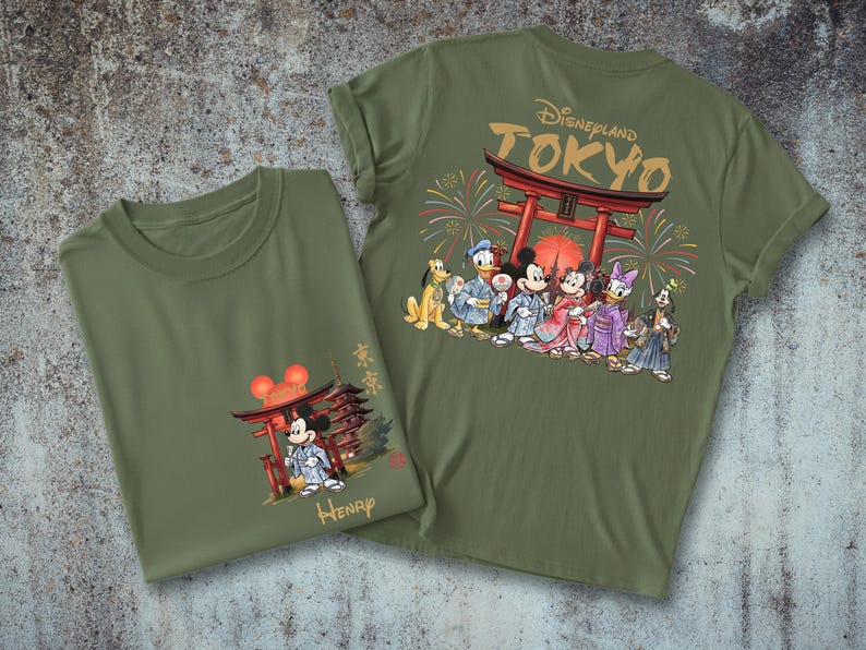 May include: Two olive green t-shirts. One features Mickey Mouse in a kimono in front of a Japanese pagoda. The other has a Disneyland Tokyo design with Disney characters in kimonos, fireworks, and a red torii gate.