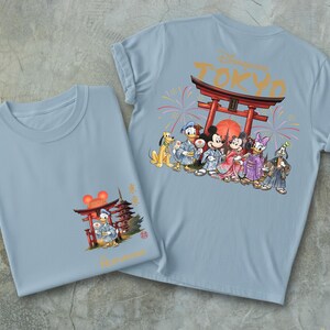 May include: Two light blue t-shirts with graphics. One shirt features a graphic of Mickey Mouse, Donald Duck, and other Disney characters in traditional Japanese attire in front of a red torii gate. The other shirt has a similar design.