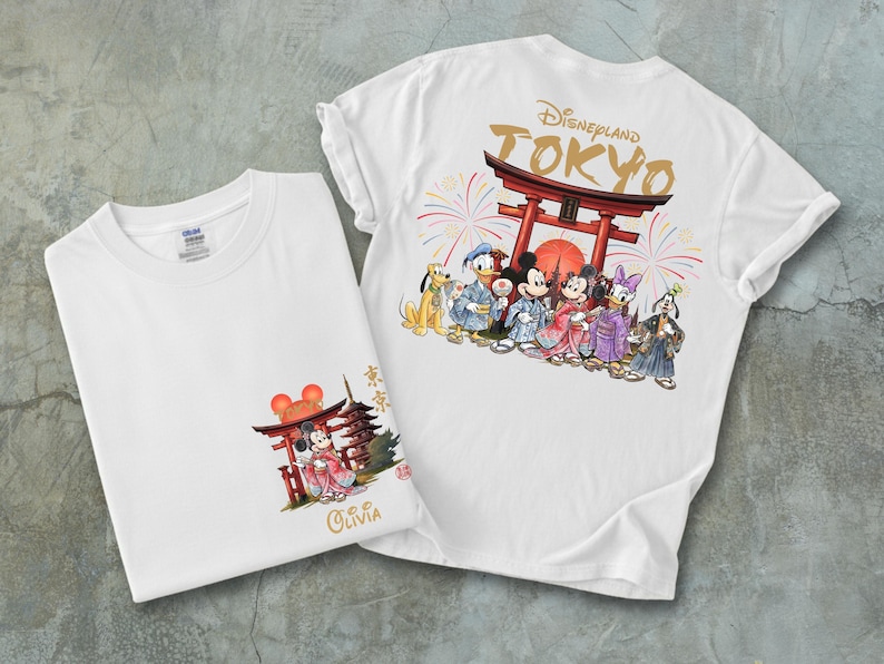 May include: Two white t-shirts with colorful graphics. One shirt features Mickey and Minnie Mouse in traditional Japanese attire in front of a red torii gate. The other shirt has the Disneyland Tokyo logo and various Disney characters in Japanese clothing.