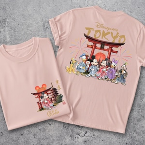 May include: Two light pink t-shirts. One shirt features a graphic of Mickey and Minnie Mouse in traditional Japanese attire, with a Torii gate. The other shirt has the text "Disneyland Tokyo" and a group of Disney characters in Japanese clothing.