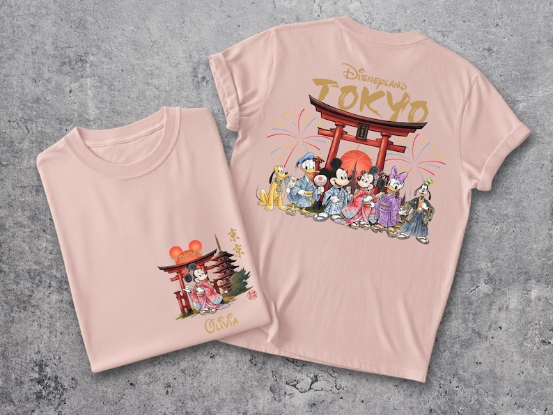 May include: Two light pink t-shirts. One shirt features a graphic of Mickey and Minnie Mouse in traditional Japanese attire, with a Torii gate. The other shirt has the text "Disneyland Tokyo" and a group of Disney characters in Japanese clothing.