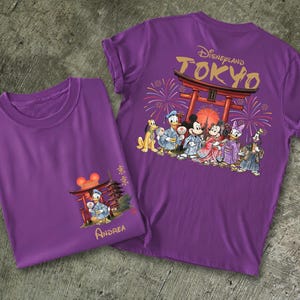 May include: Two purple t-shirts featuring Disney characters in traditional Japanese attire. One shirt has a front graphic of Donald Duck and a Japanese structure, the other has a back graphic with the text "Disneyland Tokyo" and more characters.