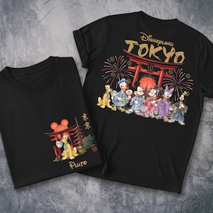 May include: Two black t-shirts featuring Disney characters in traditional Japanese attire. One shirt displays Pluto with a pagoda and the word "Pluto". The other shirt shows Mickey, Minnie, Donald, Daisy, and Goofy with "Disneyland TOKYO" and fireworks.