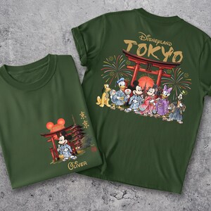 May include: Two dark green t-shirts with Japanese-themed Disney graphics. One shirt features Mickey Mouse in a kimono with a pagoda, the other has a Disneyland Tokyo design with various Disney characters in traditional Japanese attire.