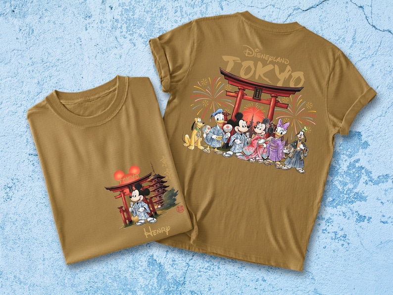 May include: Two tan t-shirts featuring Disney characters in traditional Japanese attire. One shirt shows Mickey Mouse in front of a pagoda, the other displays the characters with the text "Disneyland TOKYO" and a Japanese Torii gate.