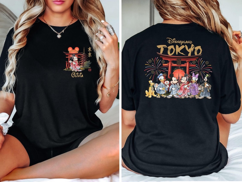 May include: Black t-shirt featuring a front graphic of Mickey Mouse in a kimono, with Japanese text and the name "Olivia." The back displays "Disneyland TOKYO" with Disney characters in traditional Japanese attire, fireworks, and a torii gate.