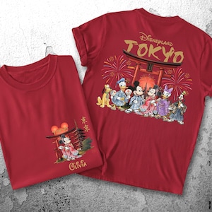 May include: Two red t-shirts. One features a graphic of Mickey Mouse in traditional Japanese attire with the text "Olivia". The other shirt has "Disneyland TOKYO" and Disney characters in Japanese clothing.