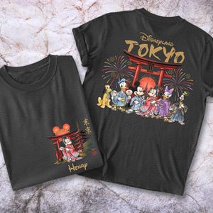May include: Two dark gray t-shirts. One features a graphic of Disney characters in traditional Japanese attire in front of a red torii gate with the text "Disneyland TOKYO". The other shirt has a smaller graphic of Mickey Mouse in front of a torii gate.