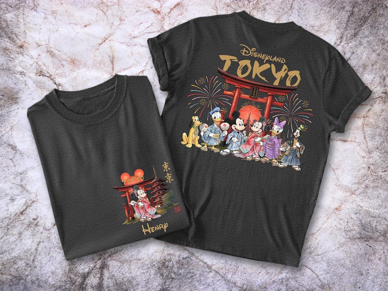 May include: Two dark gray t-shirts. One features a graphic of Disney characters in traditional Japanese attire in front of a red torii gate with the text "Disneyland TOKYO". The other shirt has a smaller graphic of Mickey Mouse in front of a torii gate.
