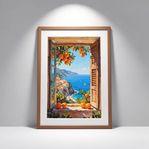 Op de afbeelding: Een ingelijste kunstdruk toont een kustscène door een open raam. Het kunstwerk toont een helderblauwe zee, witte gebouwen en sinaasappels. De raamkozijn is bruin en de stijl doet denken aan een olieverfschilderij.
