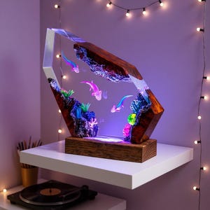 Op de afbeelding: Een verlichte hars sculptuur met een onderwater scène met axolotls en koraal. Het kunstwerk is geplaatst in een houten frame en basis. De sculptuur is ontworpen als decoratief stuk.