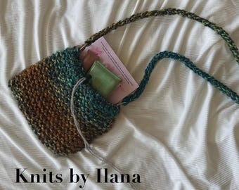 May include: A knitted purse with a strap, featuring a blend of teal, brown, and green yarn. The text "The Summer Purse" and "Knits by Ilana" are visible. The purse contains a book and a small green item.