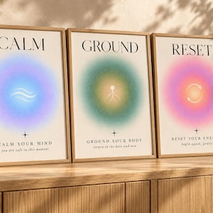 Op de afbeelding: Drie ingelijste wandposters met gradiënt aura-cirkels. De eerste toont CALM, de tweede GROUND en de derde RESET. Elk bevat kleine iconen en tekst: CALM YOUR MIND, GROUND YOUR BODY en RESET YOUR ENERGY met aanvullende zinnen.