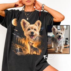 以下が含まれることがあります： チャコールグレーの半袖Tシャツで、小さなテリア犬の大きなグラフィックプリントが施されています。デザインには、滝、月、星のある森の風景の中に立つ犬の小さな姿と、その上に犬の大きなポートレートが描かれています。