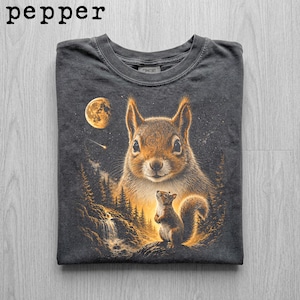 May include: Dark gray t-shirt featuring a detailed illustration of two squirrels in a forest scene under a full moon. The word "pepper" is printed at the top left. The shirt has a crew neck.