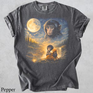 May include: Dark gray t-shirt featuring a detailed illustration of two monkeys in a moonlit forest scene. The design includes a large full moon, a waterfall, and a smaller monkey hugging a stuffed animal. The shirt is labeled "Pepper".