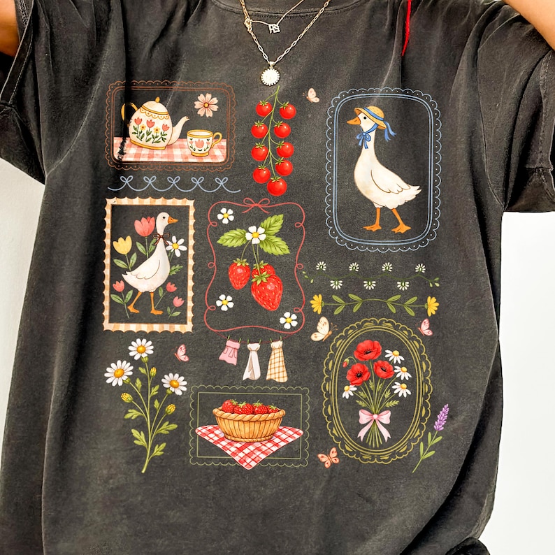 Pode incluir: Camiseta cinza escuro com uma colagem de ilustra&ccedil;&otilde;es. O design inclui uma chaleira, morangos, um ganso usando um chap&eacute;u, flores e uma cesta de morangos. As ilustra&ccedil;&otilde;es s&atilde;o emolduradas com bordas decorativas.