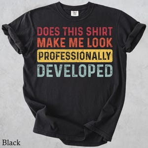 May include: A black short-sleeved t-shirt featuring distressed-style text in red, orange, yellow, and light blue. The graphic reads: DOES THIS SHIRT MAKE ME LOOK PROFESSIONALLY DEVELOPED. The shirt has a crew neckline and a standard fit.