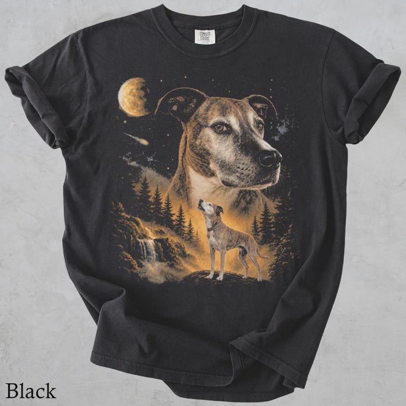May include: A black short-sleeved t-shirt featuring a graphic print of a dog's face in the night sky above a smaller dog standing on a rock near a waterfall and pine trees. The scene includes a glowing moon and stars in shades of gold and brown.